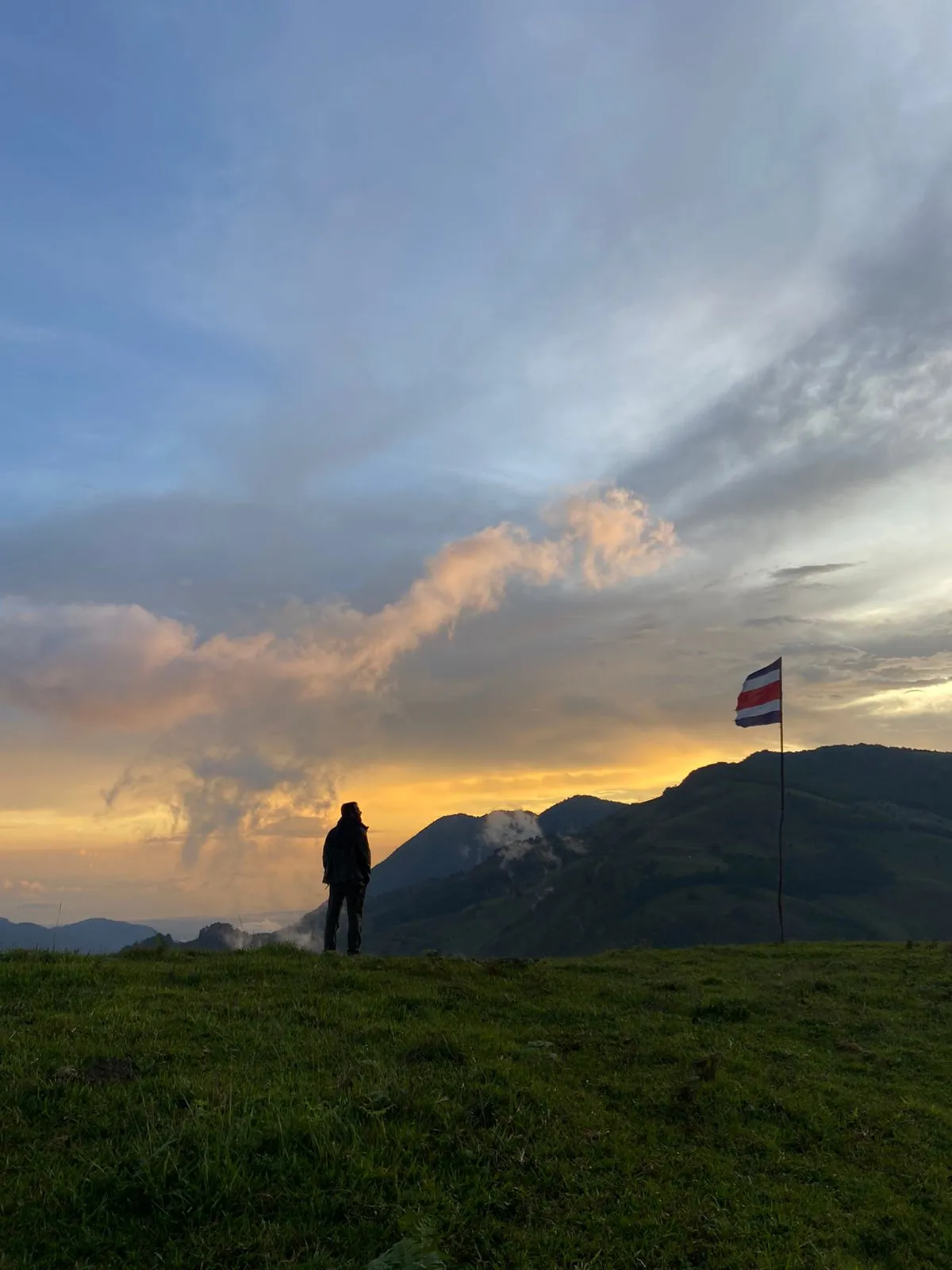Man standing next to the Costa Rica flag and looking at the mountains.