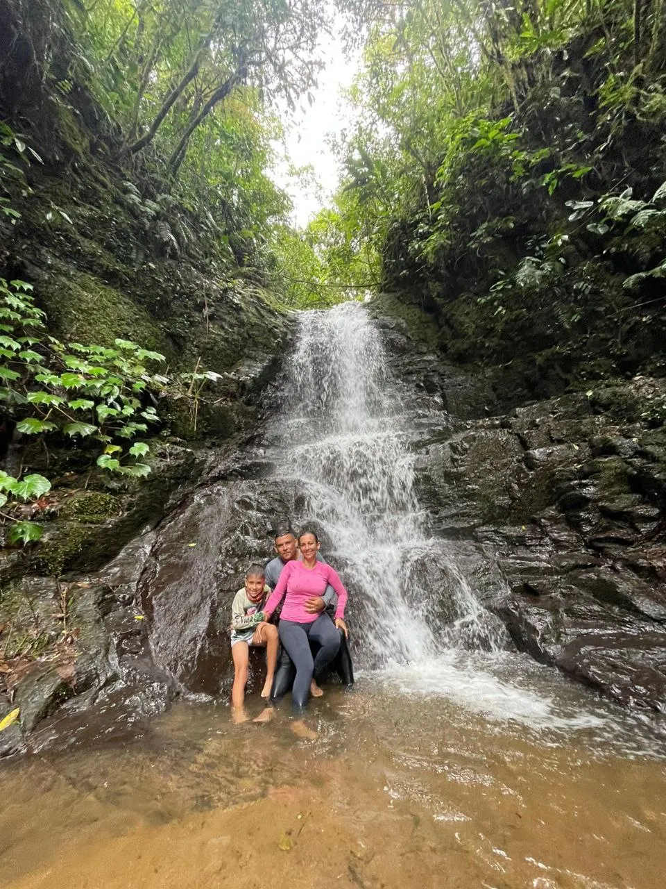 man, woman, and child smiling in front of a waterfall
